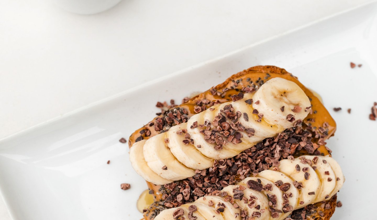 Bananaland Toast — local sourdough with peanut butter, sliced bananas, cacao nibs, and a honey drizzle